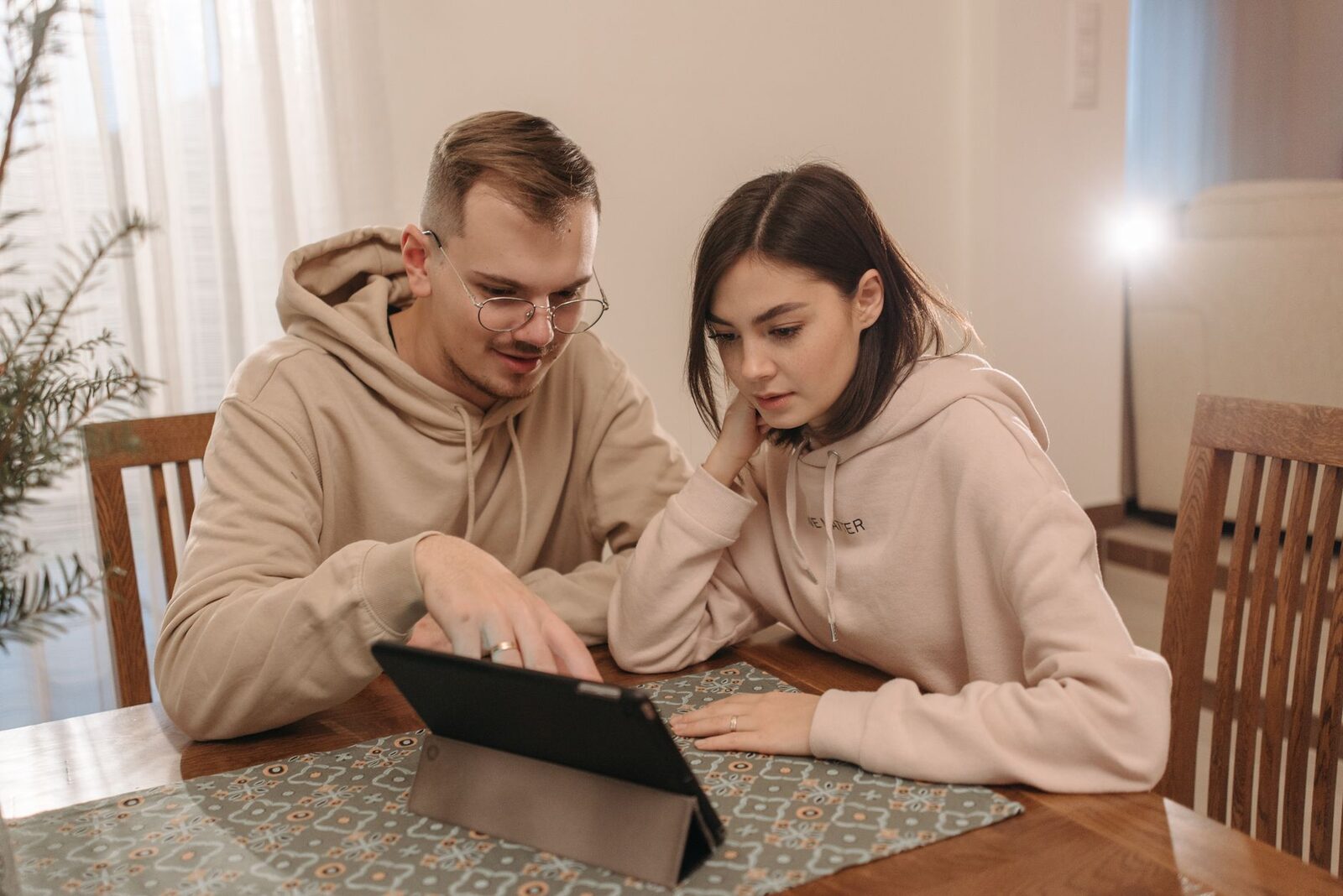 Young couple in hoodies browsing on a tablet together at home.