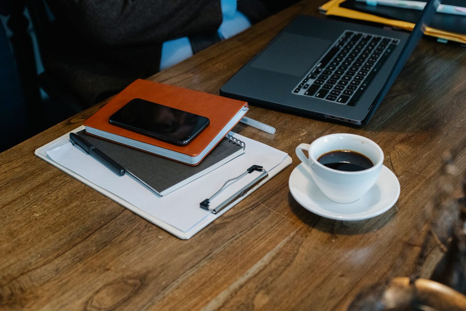 From above of opened laptop with cup of coffee placed on wooden table near notebooks and smartphone in office